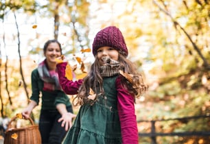 A portrait of toddler girl with mother in forest in autumn nature, having fun.