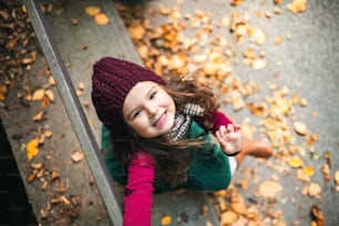 A portrait of a small toddler girl sitting in park in autumn nature, looking up. A top view.