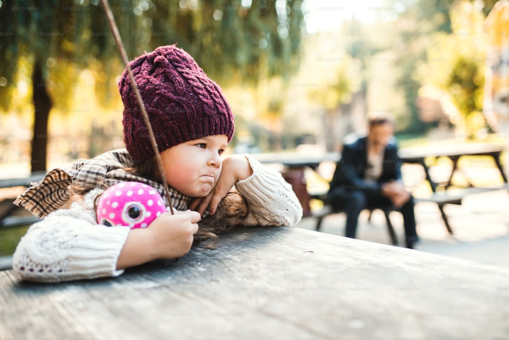 秋の自然の中で公園に座っている退屈な小さな幼児の女の子のポートレート。