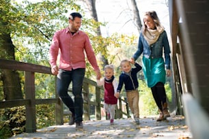 작은 쌍둥이를 데리고 손을 잡고 가을 숲을 산책하는 아름다운 젊은 가족.