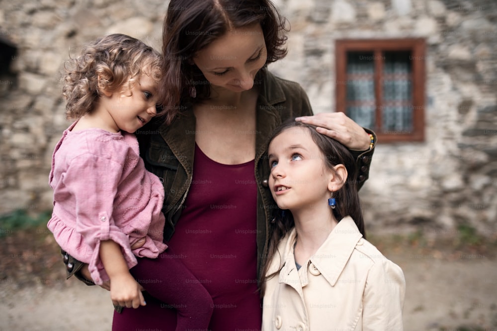 古い石造りの家の前に立っている2人の小さな娘を持つ幸せな母親。