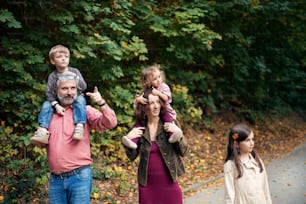 A beautiful young family with small children on a walk in autumn forest, piggyback ride.