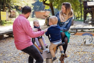 A beautiful young family with small twins playing on playground in autumn.
