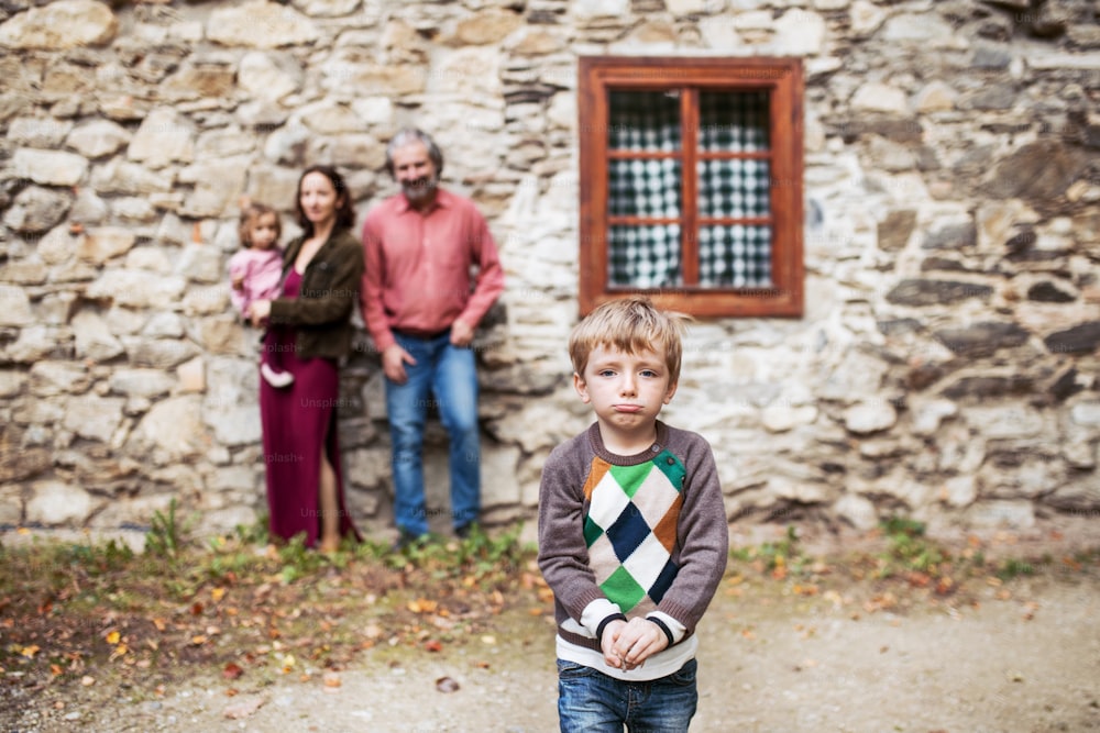 A portrait of small boy with his family standing in front of old stone house.