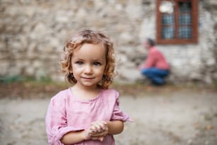 A small girl standing in front of old stone house, looking at camera. Copy space.