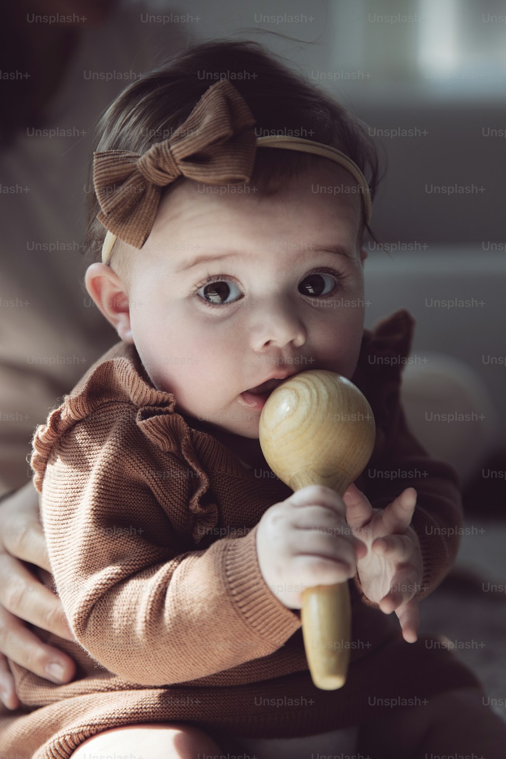 uma menina segurando um brinquedo de madeira em sua boca