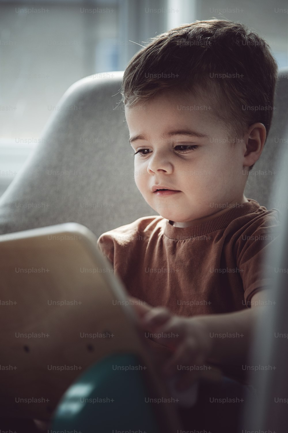 a young boy sitting in a chair looking at a tablet