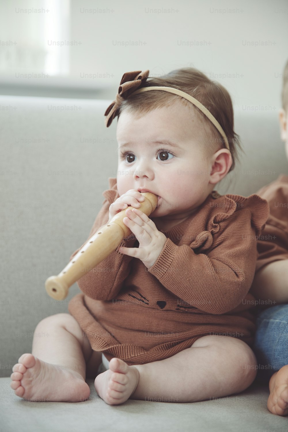 a baby girl sitting on a couch with a baseball bat in her mouth