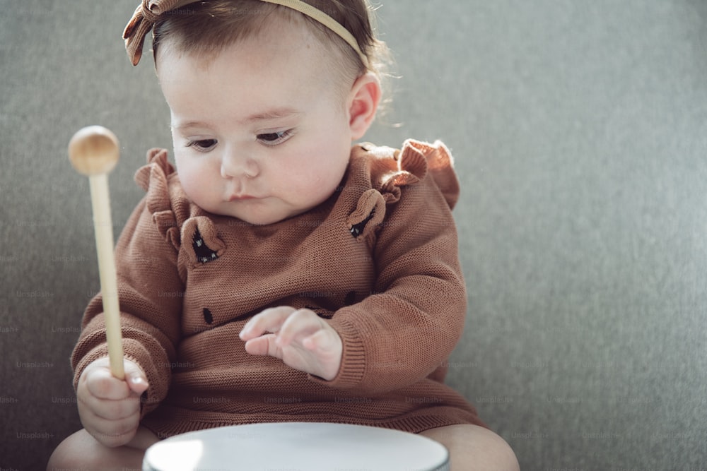 a baby sitting on a chair holding a wooden stick