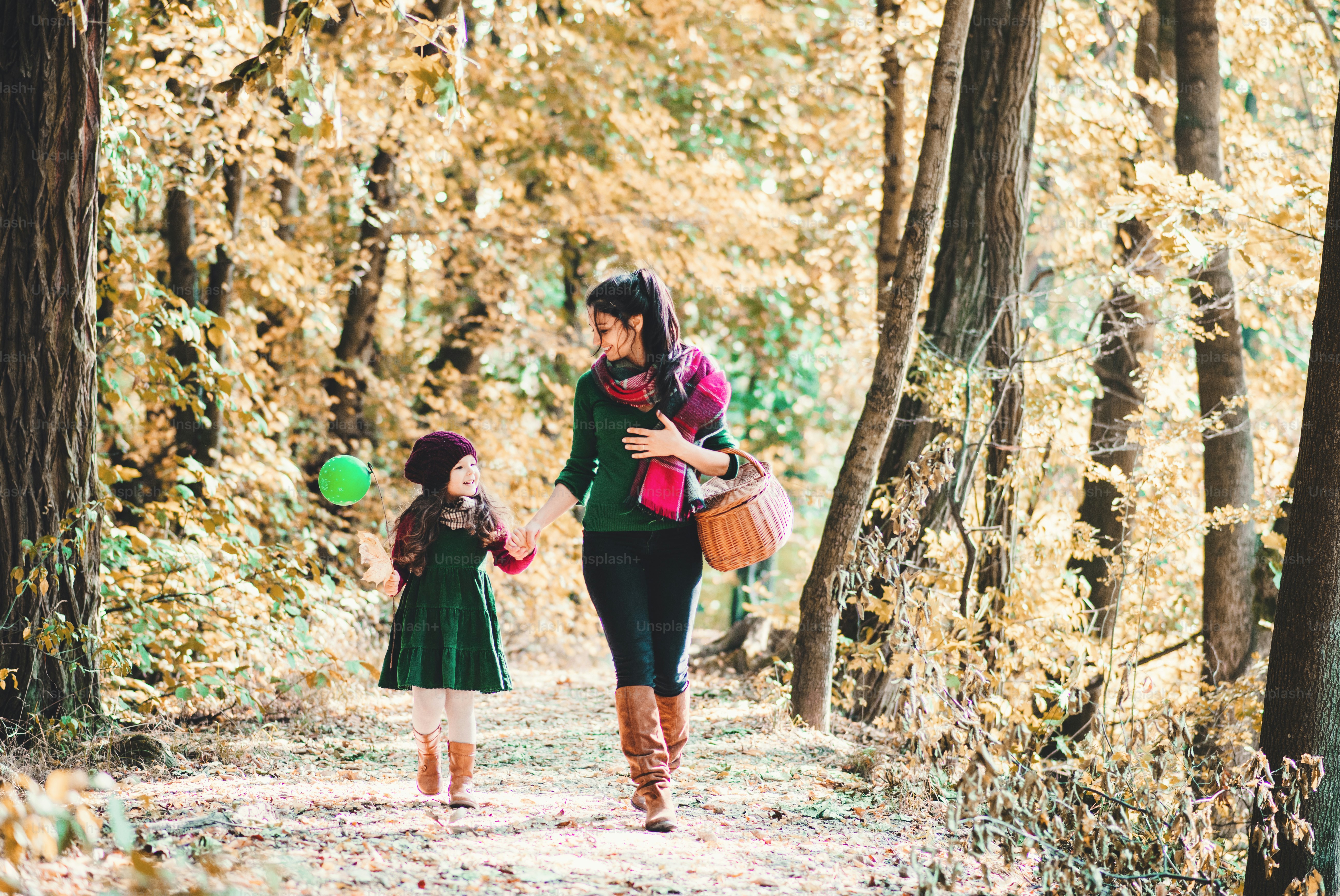 A portrait of young mother with a toddler daughter walking in forest in autumn nature, holding hands.