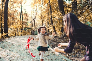 A portrait of young mother with a toddler daughter running in forest in autumn nature.