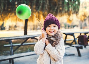 A portrait of a small toddler girl holding balloon in park in sunny autumn nature.