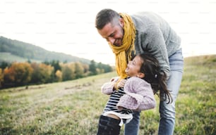 秋の自然の中で小さな娘を抱き、楽しんでいる若い父親の背面図。