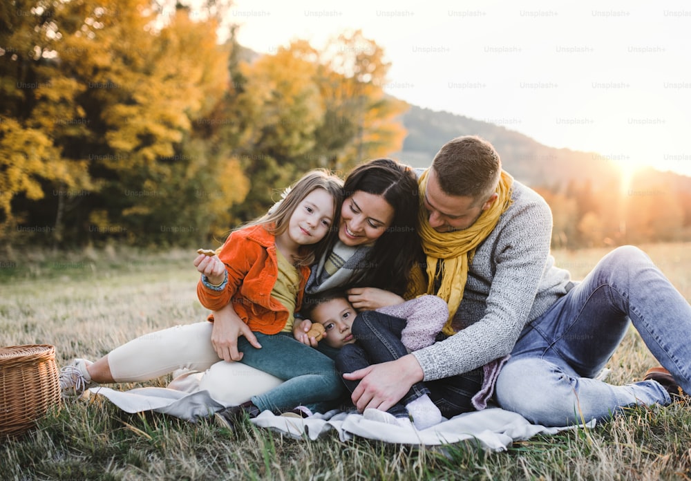 A portrait of happy young family with two small children sitting on a ground in autumn nature at sunset.