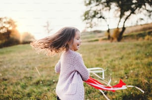 Una niña pequeña feliz jugando con una cometa de mano de arco iris en la naturaleza otoñal al atardecer.