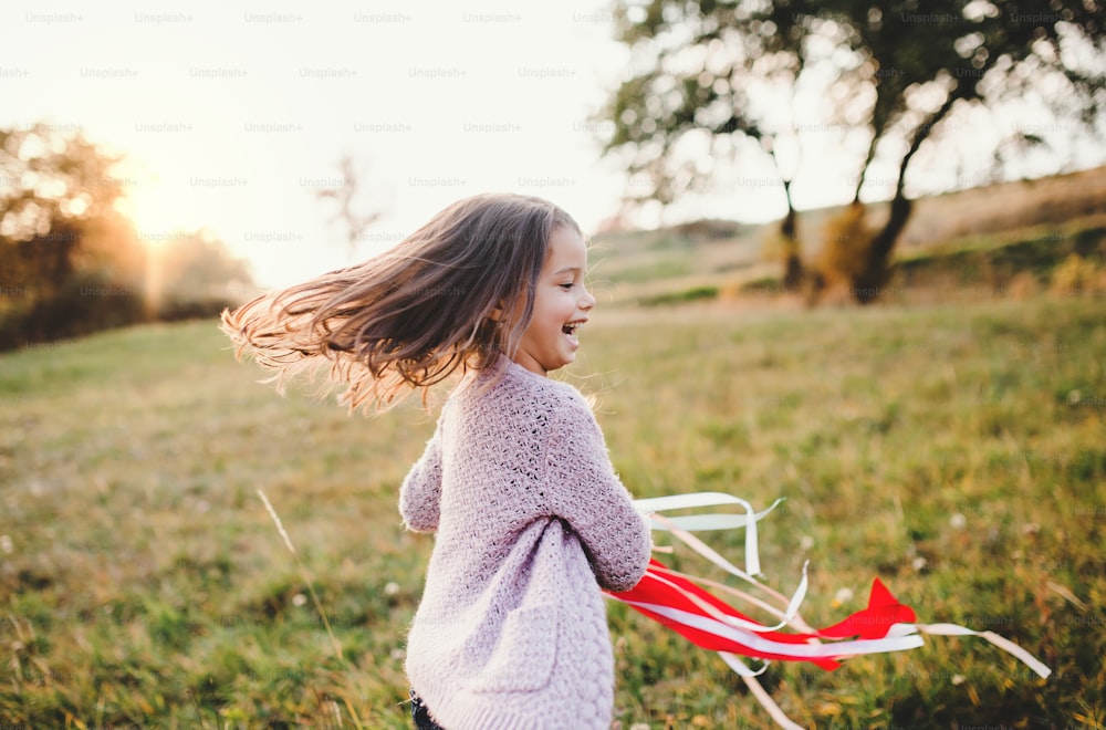 Une petite fille heureuse jouant avec un cerf-volant arc-en-ciel dans la nature automnale au coucher du soleil.