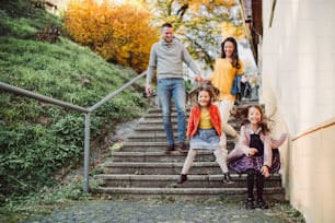 Una familia joven con una hija pequeña bajando las escaleras al aire libre en la ciudad en otoño, saltando.