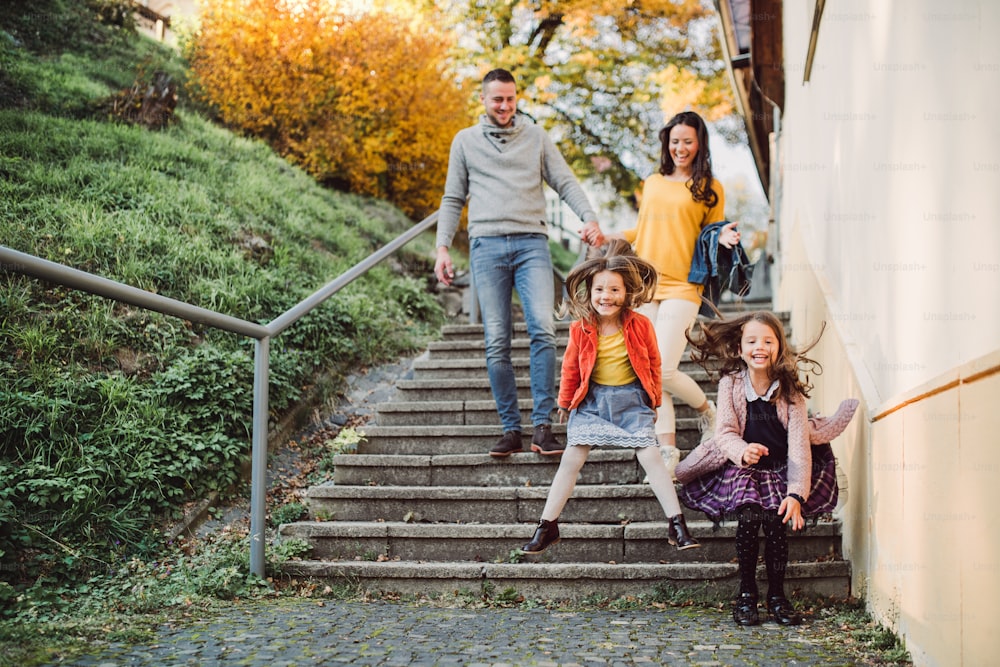 A young family with small daughter walking down the stairs outdoors in town in autumn, jumping.