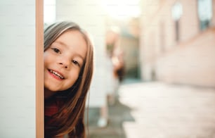 Uma garotinha feliz se divertindo na cidade no outono, olhando para a câmera.
