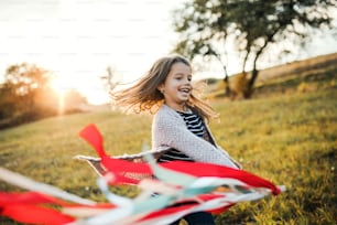 Ein glückliches kleines Mädchen, das bei Sonnenuntergang mit einem Regenbogen-Handdrachen in der Herbstnatur spielt. Speicherplatz kopieren.