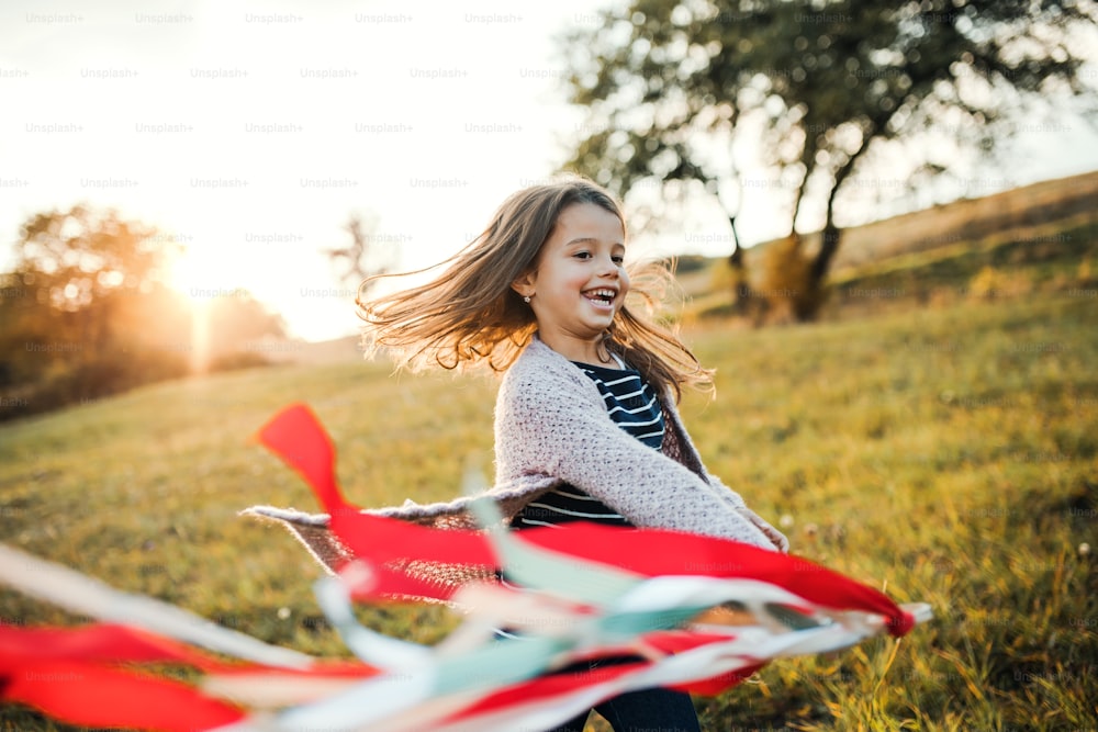 A happy small girl playing with a rainbow hand kite in autumn nature at sunset. Copy space.