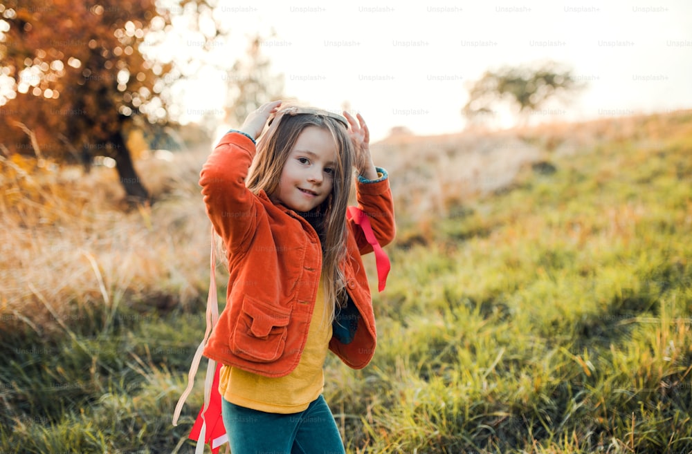 Uma menina feliz brincando com uma pipa de mão de arco-íris na natureza do outono ao pôr do sol. Espaço de cópia.
