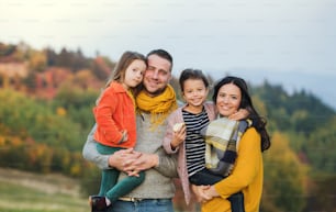A portrait of happy young family with two small children standing in autumn nature.