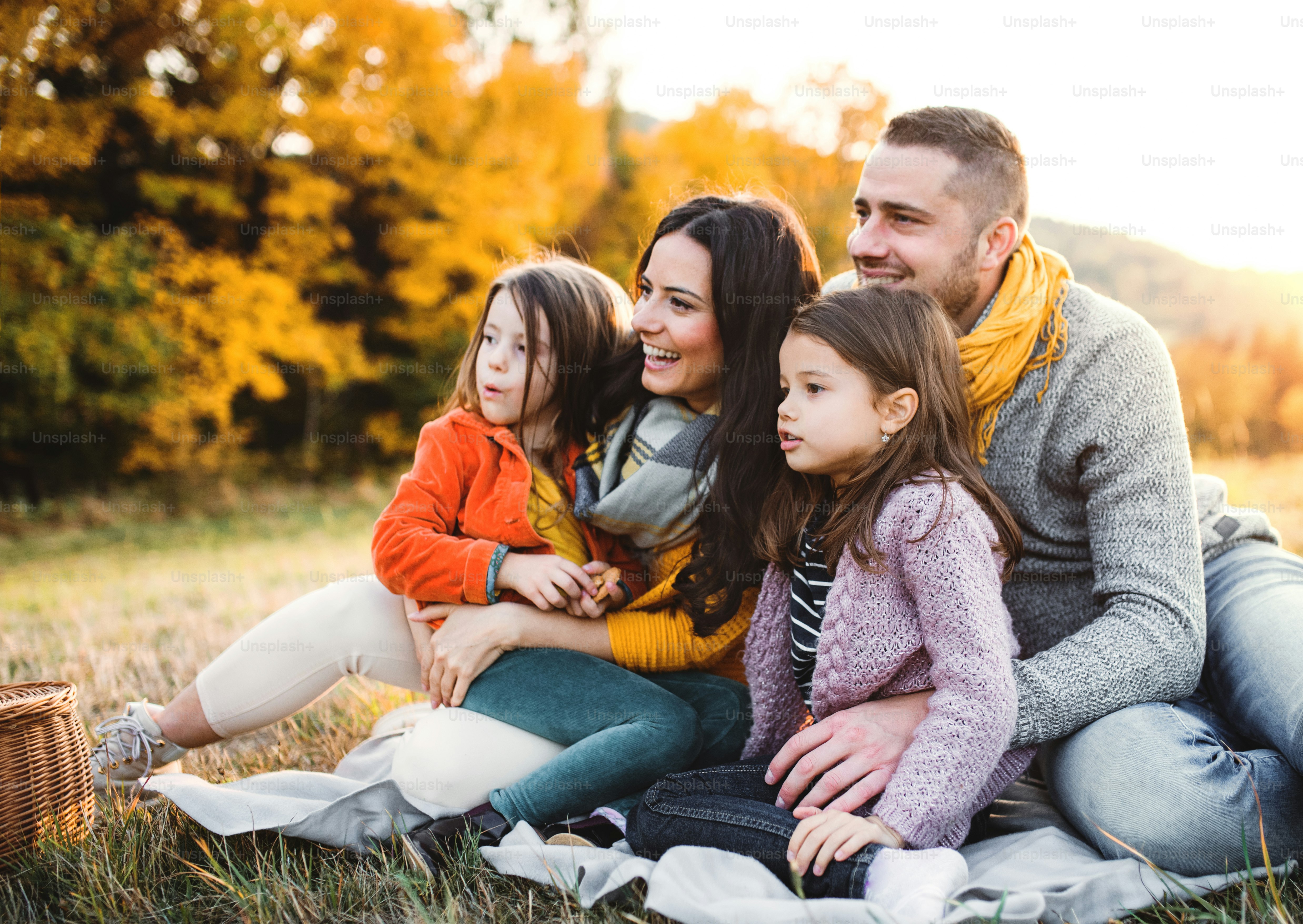 Um retrato de uma família jovem feliz com duas crianças pequenas sentadas em um chão na natureza do outono ao pôr do sol.