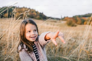 A happy small girl standing in autumn nature, pointing finger at something. Copy space.