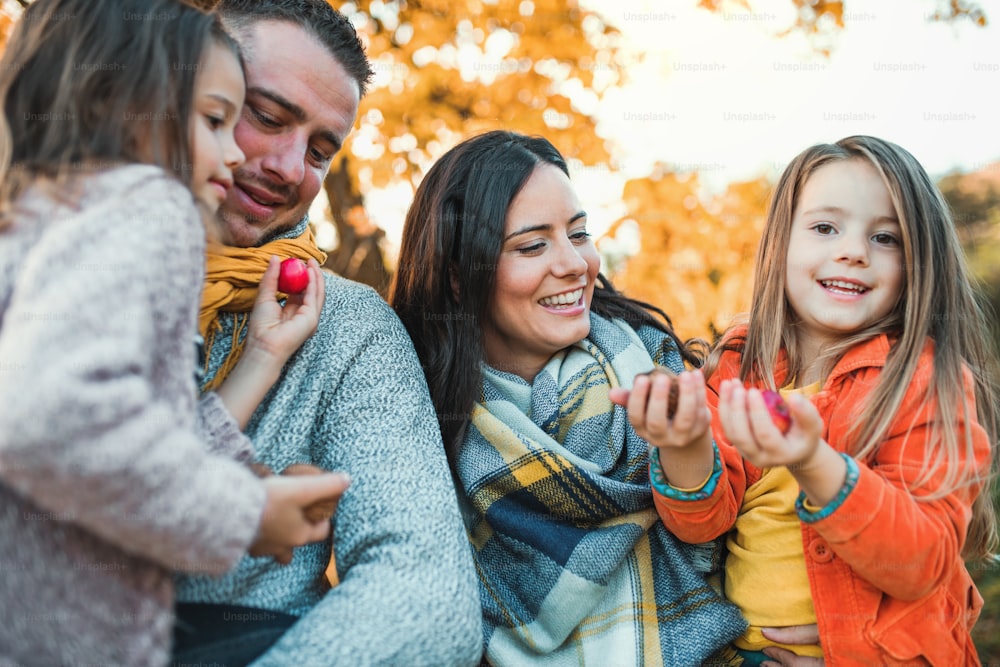 Un portrait d’une jeune famille heureuse avec deux jeunes enfants tenant des noix et des pommes dans la nature automnale.