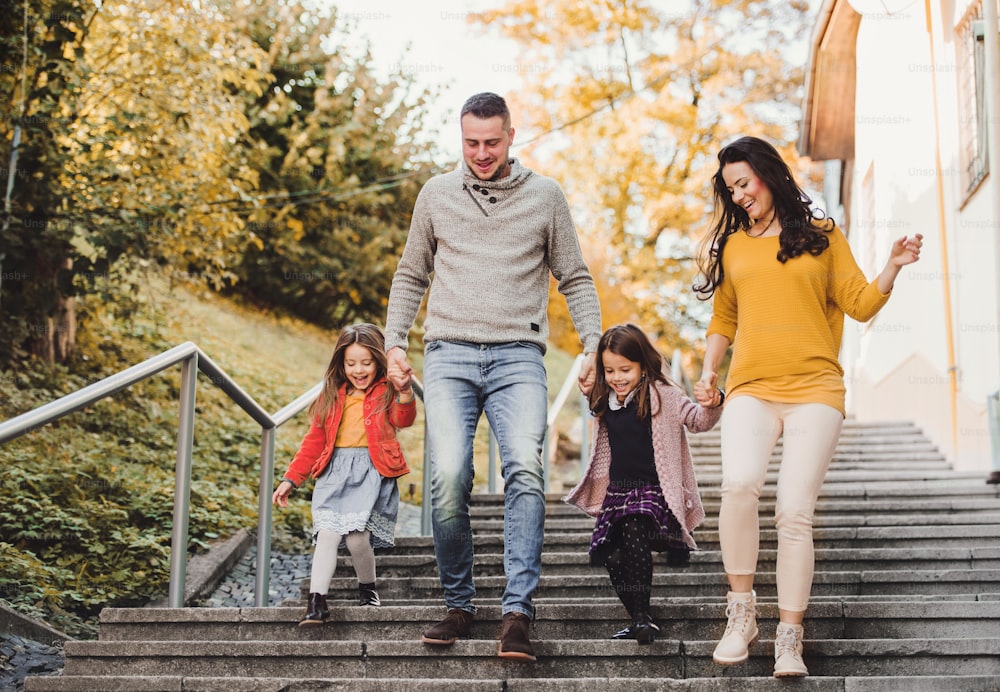 A happy young family with children walking down the stairs outdoors in town in autumn.