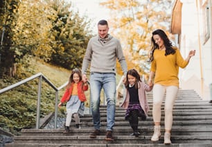 Eine glückliche junge Familie mit Kindern, die im Herbst im Freien in der Stadt die Treppe hinuntergeht.