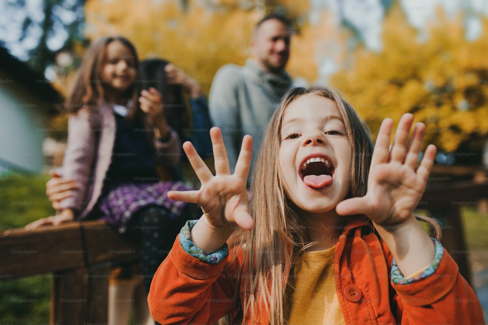 Un ritratto di bambina felice con la sua famiglia in città in autunno, sporgendo la lingua.