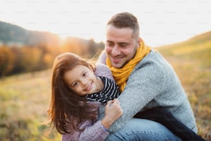 A young father holding a small daughter in autumn nature, having fun.