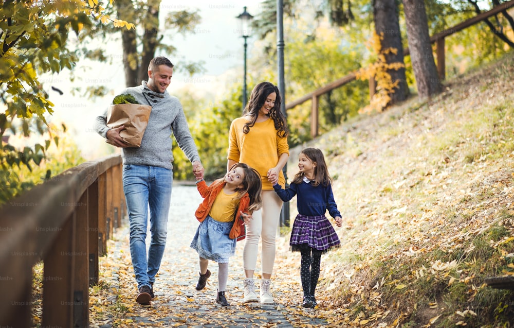 A young family with two children walking down a path in park in autumn.