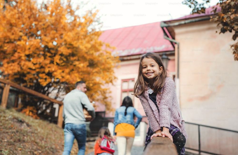 A happy portrait of small girl with her family in town in autumn, sitting on a wooden railing.