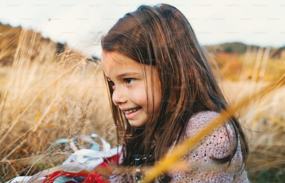 Una niña pequeña feliz jugando con una cometa de mano de arco iris en la naturaleza otoñal.