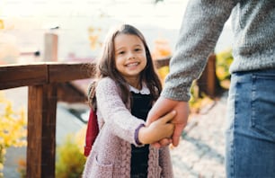 A small girl holding a hand of an unrecognizable father on a walk in sunny autumn.