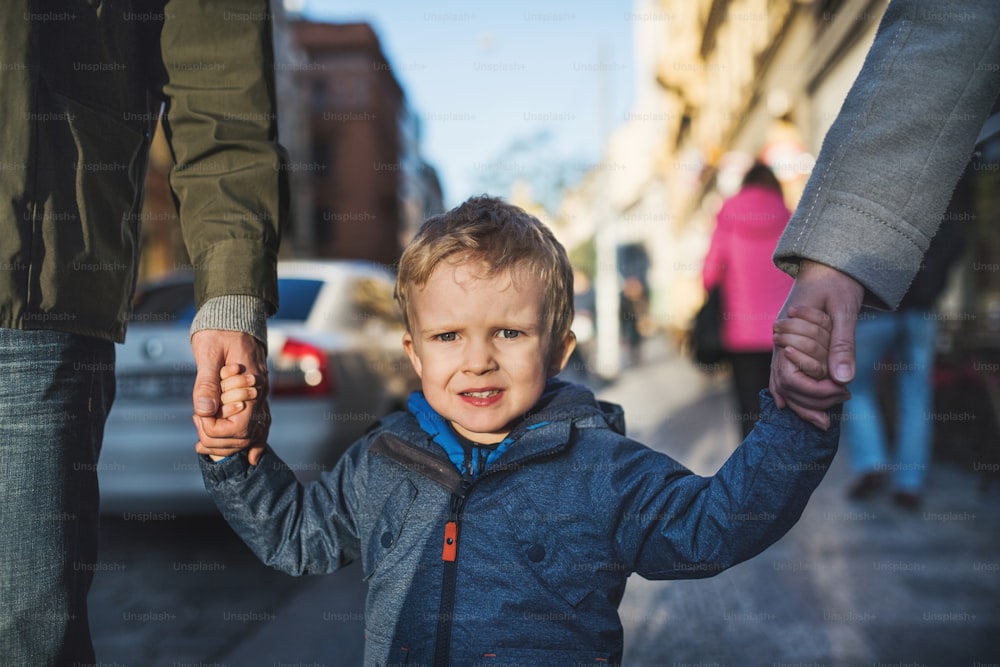 알아볼 수 없는 부모를 둔 작은 소년이 손을 잡고 도시에서 야외를 걷고 있다.