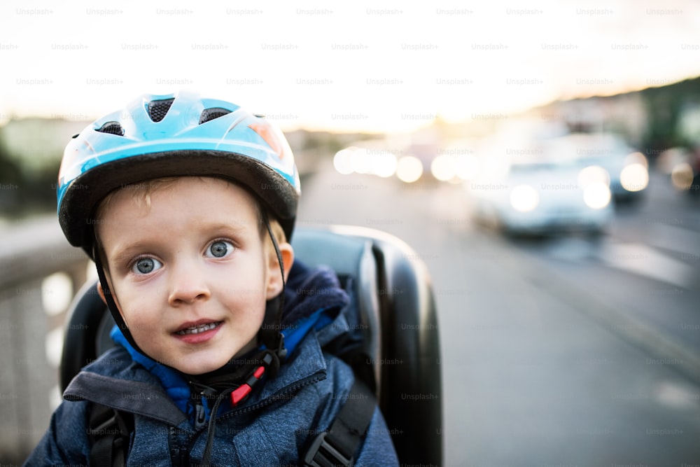 Un primer plano de un niño pequeño sentado en el asiento de la bicicleta al aire libre en la ciudad. Espacio de copia.