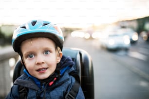 A close-up of small toddler boy sitting in bicycle seat outdoors in city. Copy space.