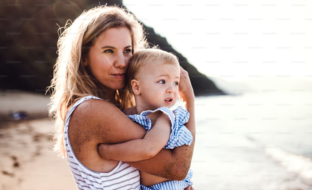 Uma jovem mãe feliz com uma menina pequena na praia nas férias de verão.