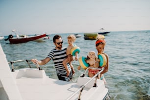 Des parents heureux avec deux petits enfants en bas âge debout près du bateau pendant les vacances d’été.