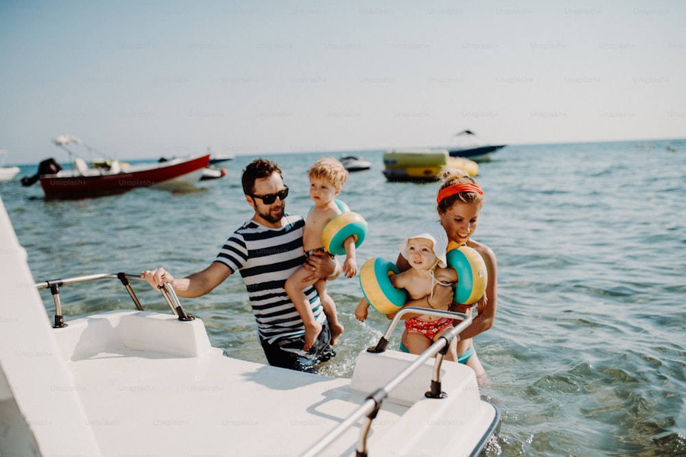 Happy parents with two small toddler children standing by boat on summer holiday.