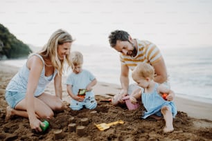 Una familia joven con niños pequeños jugando con arena en la playa durante las vacaciones de verano.