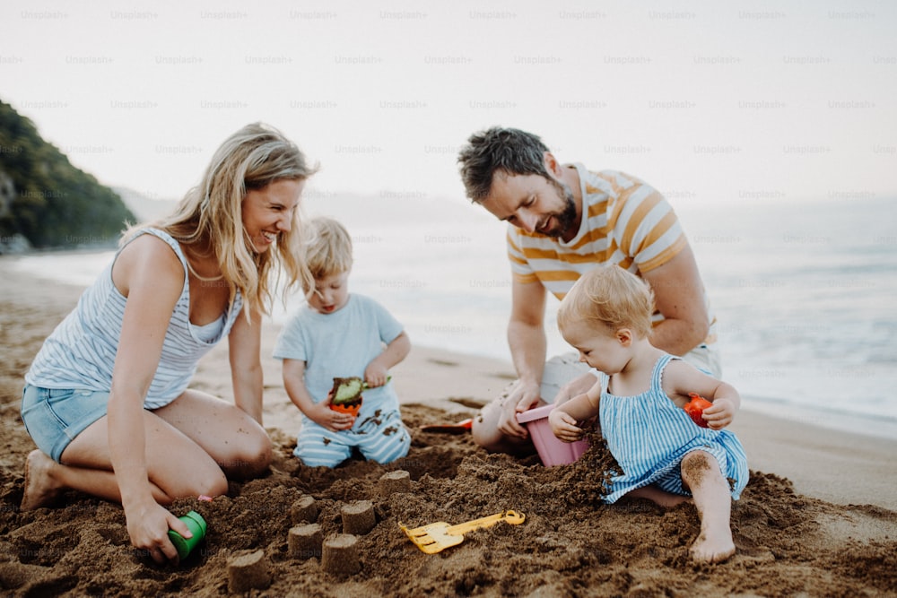Eine junge Familie mit Kleinkindern, die im Sommerurlaub mit Sand am Strand spielen.