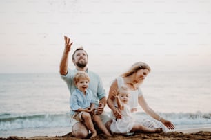 Une famille avec deux enfants en bas âge assis sur la plage de sable pendant les vacances d’été, en train de jouer.