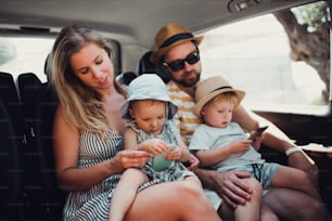 A young family with two toddler children in taxi car on summer holiday, using smartphones.