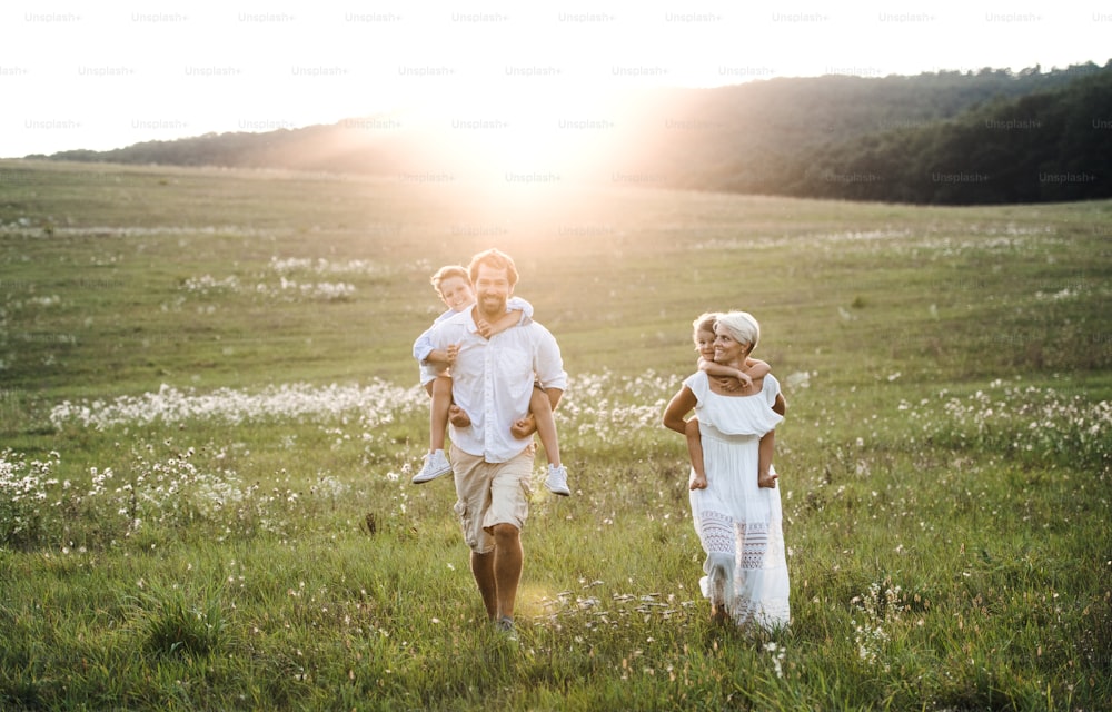 Uma jovem família com crianças pequenas caminhando em um prado ao pôr do sol na natureza de verão.