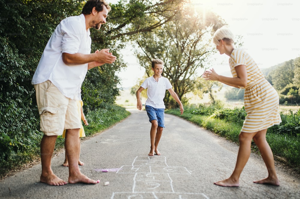 A young family with small children playing hopscotch on a road in countryside in summer.